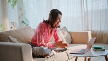 Daireden sanal konferans düzenleyen bir kadın el sallıyor. Bilgisayardan gülümseyen kadın videosu, rahat koltukta oturuyor. Oturma odasında neşeli esmer sohbet ediyor..