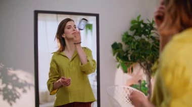 Modern apartmandaki aynada saç tarayan zarif bir kız. Şık, genç bir kadın zarif bir saç stili hazırlıyor. Hayranlık uyandırıyor. Parlak esmer, evde at kuyruğu yapıyor. Günlük rutin.