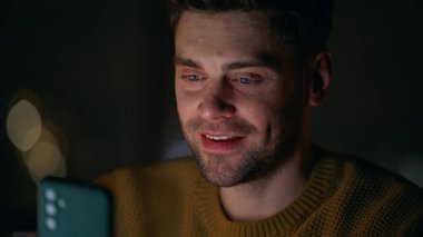 Kapanış adamı gece evde akıllı telefon gibi görünüyor. Portre gülümseyen adam karanlık dairede cep telefonundan haberleri izliyor. Cep telefonu uygulamasını kullanarak online alışveriş yaparken mutlu ol..