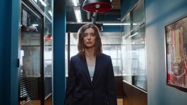 Ofiste poz veren kendine güvenen bir iş kadını kameraya özgüvenli bir şekilde bakıyor. Portre başarılı kadın yönetici modern iş merkezi koridorunda şık bir takım elbise giyerek duruyor. Kariyer konsepti.