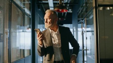 Endişeli profesyonel görünümlü cep telefonu ekranı ofis koridorunda duruyor. Gergin kıdemli işadamı koridorda e-posta okurken endişeli bir sorun yaşıyor. Salondaki akıllı telefon mesajında sakallı yönetici düşüncesi.