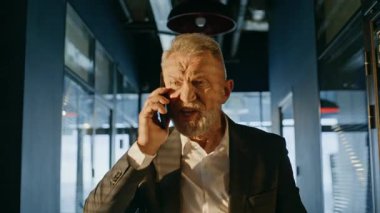Öfkeli emekli ofis koridorunda duygusal jestler yaparak konuşuyordu. Koridorda cep telefonuyla bağıran öfkeli yaşlı iş adamı. Sinirli patron, akıllı telefon görüşmesiyle astıyla çelişiyor..