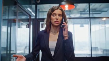 Stresli CEO cep telefonunu arıyor. Ofis koridorunda yürüyor. Yakın plan. Modern şirket koridorlarında cep telefonuyla tartışan tatminsiz bir iş kadını. Sinirli kadın patron akıllı telefon konuşmasından şikayetçi..