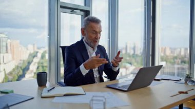 Yetenekli girişimci video araması laptopta şirket ofisindeki web kamerasında iş belgelerini gösteriyor. İnternetteki toplantıda gülümseyen kıdemli işadamı konuşuyor. Sanal sohbette Mutlu Yönetici raporu açıklıyor