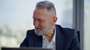 Hafif kurumsal ofiste dizüstü bilgisayara bakan yaşlı bir yönetici. Gülümseyen sakallı iş adamı dizüstü bilgisayarını kapatıyor. Başarılı yatırımcı mutlu bir şekilde işini bitirir. Profesyonel deneyim.