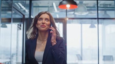 Modern ofis koridorlarında cep telefonuyla konuşan mutlu bir lider. Gülümseyen iş kadını, modern koridora çıkan ortakları arıyor. Başarılı bir bayan akıllı telefon konuşmasında kariyer tartışması yapıyor..