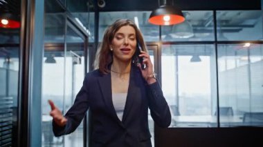 İş kadını yürüme koridoru modern ofis merkezi kapanıyor. Gülümseyen kadın yönetici şirket koridorunda cep telefonuyla konuşuyor. Pozitif kadın telefon görüşmelerinde iş detaylarını tartışıyor.