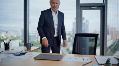 Yaşlanmış iş adamı panoramik pencerenin önünde ofis sandalyesine oturuyor. Ciddi, olgun bir yönetici bilgisayarı verimli bir iş gününe hazırlıyor. Sakallı çalışan not defterine bakıyor..