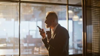 İş adamı, akşam vakti akıllı telefon yürüme salonundaki ses mesajını kaydediyor. Yönetici ofis camının yanında cep telefonundan sesli mesaj yaratıyor. Sakallı patron konuşuyor.