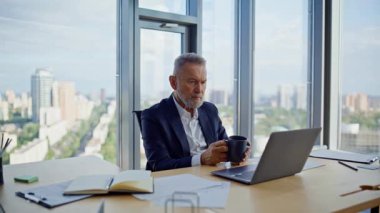 Şirket ofisinde kahve içen kıdemli girişimci yakın plan. Ciddi bir iş adamı iş yerinde içki içip dizüstü bilgisayarını karıştırıyor. İş geliştirme üzerine akıllı profesyonel düşünce mola veriyor