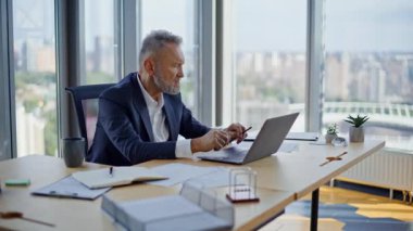 Yaşlı yönetici modern çalışma alanındaki görevleri ezip geçti. Üst düzey iş adamı, ofiste sıkı bir proje üzerinde çalışırken dizüstü bilgisayar kullanıyor. Gergin çalışan bilgisayarın kapanması iş konularına motivasyonsuz.