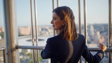 Zarif esmer, şehir manzarası tasarlıyor. Yüksek binalar inşa ediyor, balkon kapanıyor. Gülümseyen kadın yönetici, şehir manzarasına bakıyor. Tatilde ofis terasında duruyor. Mutlu iş kadını dinleniyor.