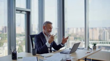 Bilgisayarlı web kamerası ile konuşan pozitif girişimci modern ofisteki kurumsal müşterilere danışıyor. Gülümseyen yaşlı iş adamı videosu arıyor. Mutlu yöneticiler çevrimiçi konferans iletişiminin keyfini çıkarın.