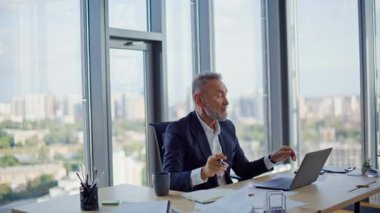 Kendine güvenen yönetici internette dizüstü bilgisayarla konuşup evrakları gösteriyor. Olgun iş adamı ofiste video toplantısında sözleşmeyi tartışır. İnternet sohbetinde belge iş verilerini gösteren zarif lider.