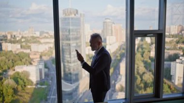 Şaşırmış ezik görünümlü cep telefonu ofis panoramik penceresinin yanında duruyor. Kıdemli müdür işyerinde umutsuzluk hisseden işten çıkarma ilanını okudu. Stresli yatırımcı cep telefonu bankacılığı uygulaması para kaybediyor