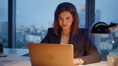 Akşam çalışan gülümseyen masturbasyoncu bilgisayarın internet sitesine yakından bakıyor. Lamba ışığında e-posta okuyan mutlu iş kadını. Başarılı bayan yönetici online proje geliştiriyor karanlık ofis çalışma alanında oturuyor.