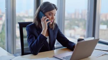 Şirketimizin iş yerinde laptopta çalışan akıllı telefonlu gülümseyen girişimci. Pozitif iş kadını telefon konuşmalarında fikirlerini paylaşıyor. Mutlu kadın CEO cep telefonuyla stratejiyi tartışıyor..