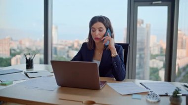 Modern iş yerinde akıllı telefondan konuşan, dizüstü bilgisayarı olan çok görevli bir kadın. Kendine güvenen bir iş kadını cep telefonuyla iş görüşmelerini tartışıyor. Ciddi bayan patron, müzakere ortaklarını arıyor..