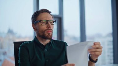 Şirket işyerindeki evrakları inceleyen profesyonel muhasebeci. Gözlüklü başarılı bir işadamı ofiste karlı bir anlaşma okuyor. Gülümseyen CEO mali belgeleri inceliyor, ellerini ovuşturuyor.