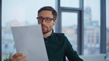 Modern çalışma alanındaki belgeleri yakından inceleyerek ciddi bir başlangıç. Stresli iş adamı memnuniyetsiz mali rapor ofiste gözlüğü çıkarıyor. Hüsrana uğramış girişimci banka kredisinin reddedilmesini okuyor