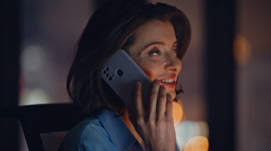 Portre işindeki kadın modern ofiste cep telefonunu arıyor. Gülümseyen iş kadını akıllı telefondan konuşuyor karanlık bir iş yerinde tek başına oturuyor. Neşeli zarif yönetici cep telefonuyla içeride haberleri tartışıyor.