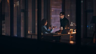 İş arkadaşları karanlık ofis alanında lamba ışığında kahve içiyorlar. Gülümseyen meslektaşlar mesai sonrası haberleri paylaşıyorlar. Ortaklar akşam geç saatlerde iş projesini tartışıyor.