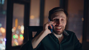 Gülen bir çalışan cep telefonu konuşmasının keyfini çıkarır. Mutlu iş adamlarının karanlık işyerlerinde hoş bir akıllı telefon iletişimi vardır. Gülümseyen adam arıyor. Harika haberleri paylaşıyorlar..