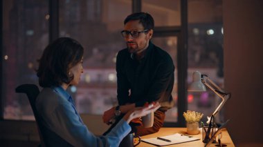 Karanlık şirket işyerinde laptopla dostça sohbet eden rahat personel. İki meslektaş, ellerinde kahve fincanları ile haberleri paylaşıyor. Sakin iş ortakları gece geç saatlerde iş fikirlerini tartışıyor