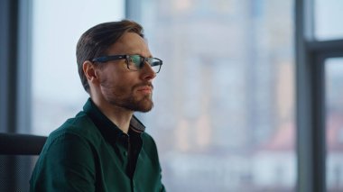 Gülümseyen müdür modern ofis alanının kapanışını gösteriyor. Başarılı iş adamı panoramik pencerenin önünde poz veren gözlük takıyor. Şirket işyerinde siyah gömlekli sakallı lider..