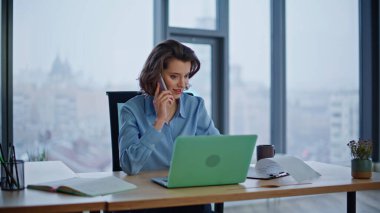 Gülümseyen iş kadını iş yerindeki gazeteleri kontrol etmek için cep telefonunu arıyor. Pozitif iş kadını cep telefonu görünümlü dizüstü bilgisayar konuşuyor. Kendine güvenen kadın yönetici, müvekkil okuyucu belgesine danışıyor.