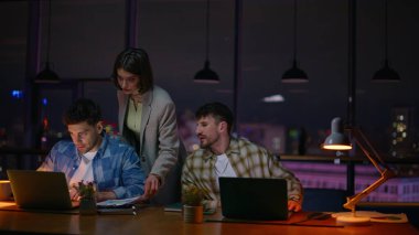 Geç kalmış takım arkadaşları yaratıcı akşam ofisinde çalışıyor. Bilgisayar işyerindeki kağıtları kontrol eden yetenekli tasarımcılar. Takım arkadaşları karanlık odada son teslim tarihini bekliyor. Birlikte dizüstü bilgisayar kullanan insanlar.