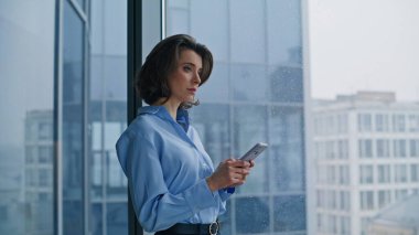 Şirket yöneticisi şık bir bluzla panoramik pencerenin yanında akıllı telefonu izliyor. İş yerindeki kendine güvenen iş kadını cep telefonu mesajını okuyor. Gülümseyen çalışanlar bankacılık uygulaması.