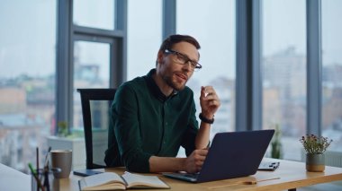 Sakallı girişimci ofis panoramik penceresindeki başarıyı düşünerek iş projesi yapıyor. Gülümseyen iş adamı dizüstü bilgisayar. İş yerinde online uygulama geliştiren profesyonel bilişim işçisi.