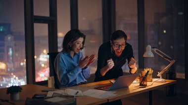 İş dünyasının başarısını kutlayan inanılmaz kazananlar gece iş yerinde bilgisayarlara göz atıyorlar. Heyecanlı iş adamları bilgisayar görüntüsü veren başarılarına seviniyor. Mutlu meslektaşlar zaferin tadını çıkarıyor.