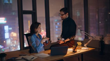Ofis ekibi gece geç saatlerde iş yerinde kahve fincanlarını tokuşturuyor. İki gülümseyen meslektaşımız mesai molasından keyif alıyor. Mutlu iş kadını iş adamı birlikte içki içiyor..
