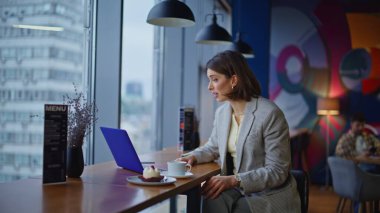 Modern kafeteryadaki bilgisayarla online çalışan zarif bir öğrenci. Resmi takım elbiseli, kendine güvenen esmer kadın kafeden arıyor. Duygusal iş kadını sanal toplantı jestinde danışmanlık yapıyor. 