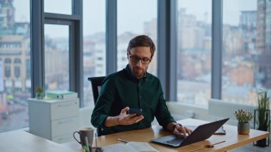 Modern çalışma alanında dizüstü bilgisayarda çalışan pozitif danışman. Zarif girişimci çağrıya cevap veriyor. Dostça iletişimin tadını çıkarın. Şirket ofisinde gülümseyen iş adamı akıllı telefon konuşuyor..