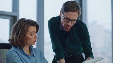 Erkek amir, şirket ofisinde kadın yöneticiyle evrakları tartışıyor. Memnuniyetsiz yönetici mali rapordan muhasebeciye şikayet ediyor. İki meslektaş iş belgelerini inceliyor.