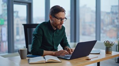 Modern ofiste laptoptan haber okuyan şaşkın iş adamı, e-postayı yakından okuyor. Heyecanlı menajer duygusal olarak online galibiyeti kutluyor. Gözlüklü mutlu yönetici evet işareti yapıyor. Sevinçten uçuyor.