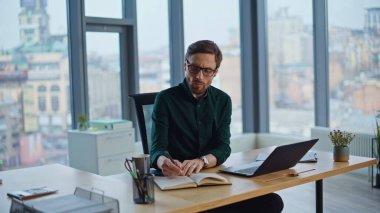 Not defterine not yazıp şirket ofisinde dizüstü bilgisayarla araştırma yapmakla meşgul. Sakallı iş adamı yaratıcı bir proje üzerinde çalışıyor. Ciddi bir girişimci içeride iş kuruyor..