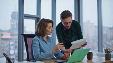 İş adamı, dizüstü bilgisayar masasında belgeleri olan kadın yöneticiye danışmanlık yapıyor. Dost canlısı bir yönetici iş arkadaşına evraklarla ilgili finansal verileri açıklıyor. Modern ofiste iki takım üyesi el sıkışıyor.