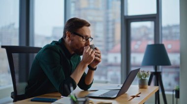 İş yerinde kahve içen rahat bir çalışan yakın çekim yapıyor. Gülümseyen sakallı iş adamı ofis işinden dinlenirken kapuçino yudumluyor. Başarılı yönetici iş fikirleri üretiyor ve duraksamanın keyfini çıkarıyor.