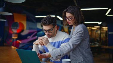 Profesyonel kadın kreatif ajans salonunda projeyi tartışıyor. Modern iş yerinde laptopla iş birliği yapan odaklanmış iş arkadaşları. Şirket toplantısında ciddi takım çalışması.