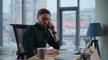 Endişeli yönetici iş yerinde cep telefonuyla konuşuyor ve dizüstü bilgisayarını kapatıyor. Endişeli iş adamı iş meselelerini cep telefonuyla açıklıyor. Sorunlu CEO 'nun gözlüklerini çıkarması sorunu akıllı telefondan tartışır..