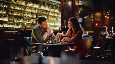 Lokantada tatlı bir çift buluşması. Gülümseyen adam kırmızı elbiseli güzel bir kadınla el ele tutuşuyor. Şefkatli ruh eşleri şarap kadehiyle bar masasında oturuyorlar. Romantik ilişki kavramı.