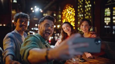 Grup arkadaşları modern barda ellerinde şarap kadehleriyle akıllı telefondan selfie çekiyorlar. Akşam buluşmasında telefonda fotoğraf çeken iki çift gülümsüyor. Barda toplanan kaygısız gençlerin fotoğraflarını çeken mutlu gençler.