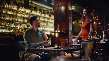 Sevgilisiyle barda buluşuyor, sarılıyor ve mutlu buluşmaların tadını çıkarıyor. Gülümseyen yakışıklı adam, menüyü alıp kıza düzen teklif ediyor. Karanlık kulüp atmosferinde çıkan pozitif bir çift. İlişki kavramı.