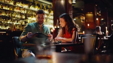 Mutlu eşler menüde romantik bir akşam geçiriyorlar. Gülümseyen adam kırmızı elbiseli güzel bir kadına yemek teklif ediyor. Mutlu çift gece barında buluşmanın tadını çıkarıyor..