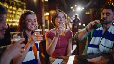 Spor hayranları yakın planda televizyon seyrederek bira tokuşturuyor. Birlikte futbol takımını destekleyen gülümseyen arkadaşlar hafta sonları eğleniyorlar. Mutlu gençler alkol içerek TV maçına odaklanıyor.