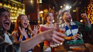 Heyecanlı öğrenciler, modern barda spor oyunu oynuyorlar ve yakın plan bira içiyorlar. Bar televizyonunda maç izleyen mutlu grup taraftarları. Neşeli arkadaşlar kadehleri tokuşturur gecenin tadını çıkar.